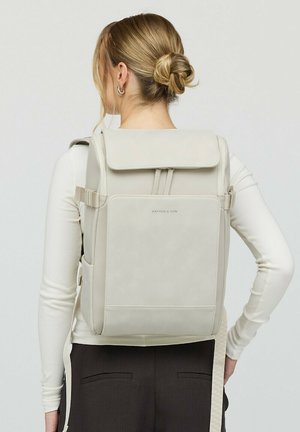 Lichtbeige rugzak gemaakt van zacht stof met een klepopening, verstelbare schouderbanden, een voorvak en subtiele logo-details.