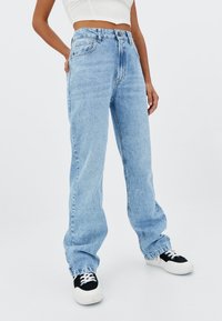 Jeans dritti azzurri chiari con vita alta, design classico a cinque tasche e lieve sbiadimento. Abbinati a sneakers nere e bianche.