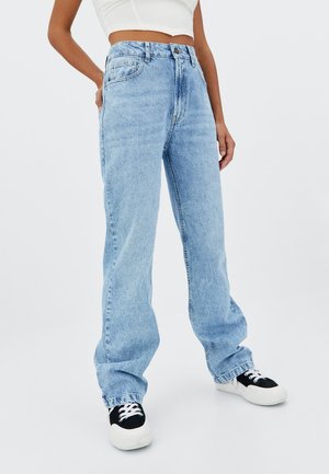 Light blue straight-leg jeans with a high waist, classic five-pocket design, and slight fading. Paired with black and white sneakers.