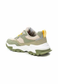 Zapatilla de running verde y beige con materiales de malla y ante, suela de tracción blanca, cuello acolchado y acentos amarillos en los cordones y el talón.