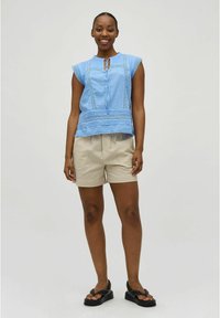 Lichtblauwe katoen blouse met kapmouwen, kantdetails en striknek, gecombineerd met beige shorts en zwarte sandalen. Eenvoudig ontwerp.