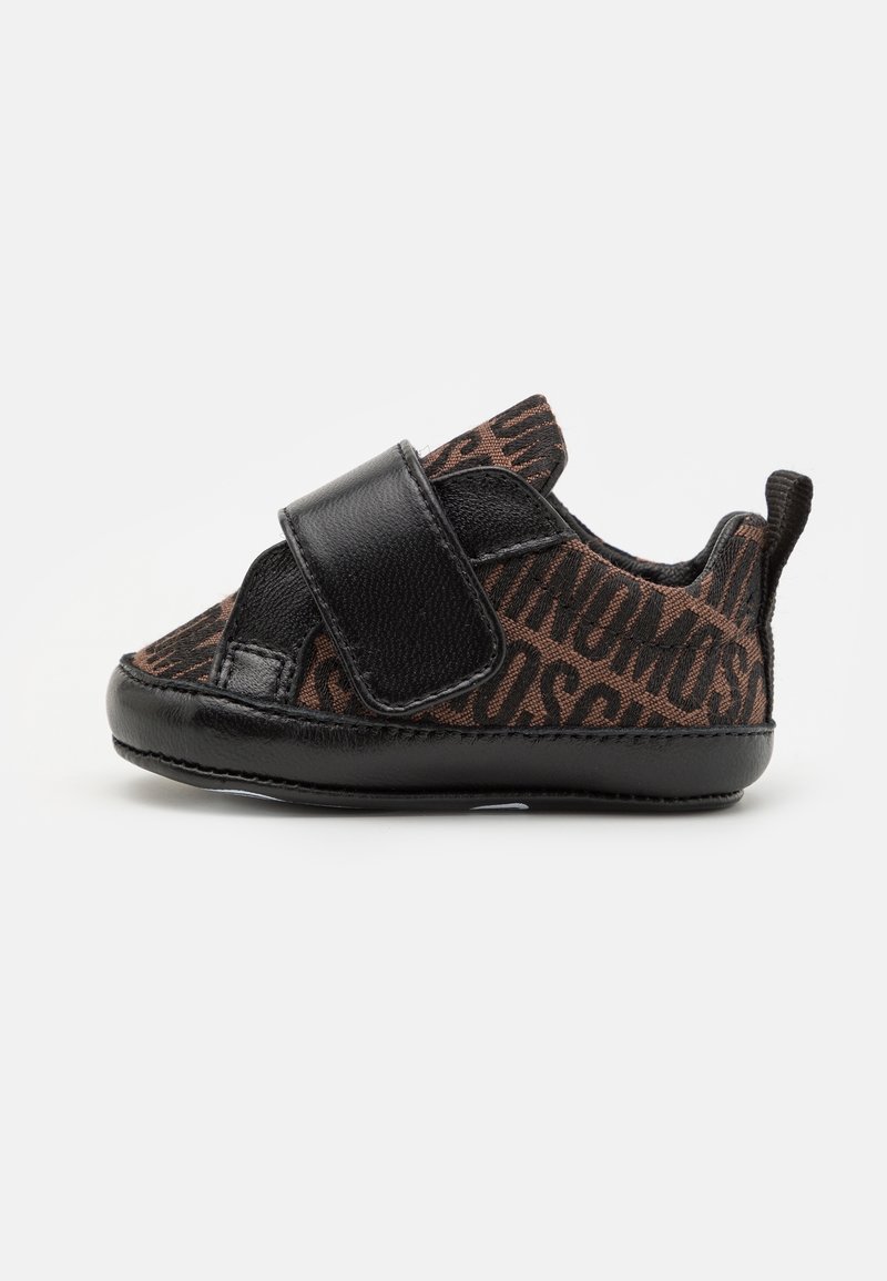 Petite chaussure de bébé noire et marron avec un motif de texte imprimé, large bride en Velcro noire et semelle souple sur un fond blanc uni.
