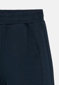 Marineblå svedbukser lavet af blødt stof, med elastisk talje, sidelommer og broderet logo på venstre lår.