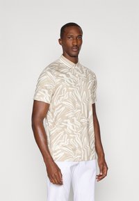 Kurzärmliges Poloshirt in Beige mit weißem abstraktem Muster, mit einem Kragen und glatter Textur.