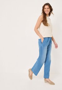 Top sin mangas color beige claro y pantalones de mezclilla sueltos color azul claro, con bolsillos laterales, combinados con alpargatas de esparto color marrón claro.