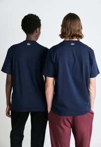 Tricouri din bumbac de culoare bleu marin, cu mâneci scurte, având un mic logo verde pe gulerul din spate. Croială casual, asortate cu pantaloni închis și bordeaux.
