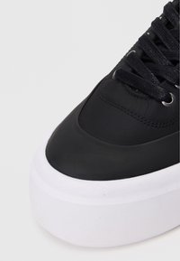 Μαύρο αθλητικό παπούτσι με ματ επάνω μέρος, παχιά λευκή σόλα και επίπεδες μαύρες κορδόνες. Διακριτές ραφές περιμετρικά.