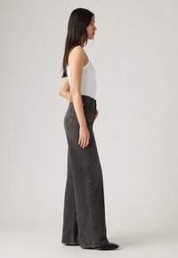 Jean taille haute, jambe large en denim noir délavé avec une silhouette droite, dotée d'une fermeture à boutons et de poches arrière discrètes.