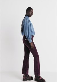 Denimskjorte med lange ermer, kombinert med bordeaux cordfløyelsbukser med vide ben og kraftige svarte støvler. Enkelt design med diskrete sømdetaljer.