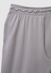 Helle graue Jogginghosen mit elastischem Bund, die eine glatte Textur und eine Seitentasche aufweisen. Das Design legt den Fokus auf Komfort und Praktikabilität.