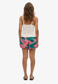 Top di cotone all'uncinetto bianco con spalline regolabili, abbinato a pantaloni corti rosa con modelli di foglie tropicali verdi. Tessuto morbido; vestibilità casual.