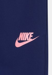 Námořnické modré Nike tepláky s výrazným růžovým logem na levém stehně, vyrobené z měkké tkaniny s hladkým povrchem.