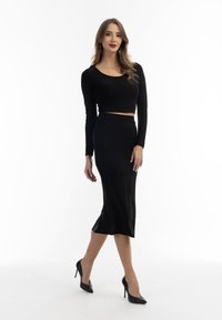 Fekete, női rövid ujjú crop top, hosszú ujjal, fekete karcsú midi szoknyával párosítva. Sima textura, testhez simuló forma, amelyet magas sarkú cipők egészítenek ki.