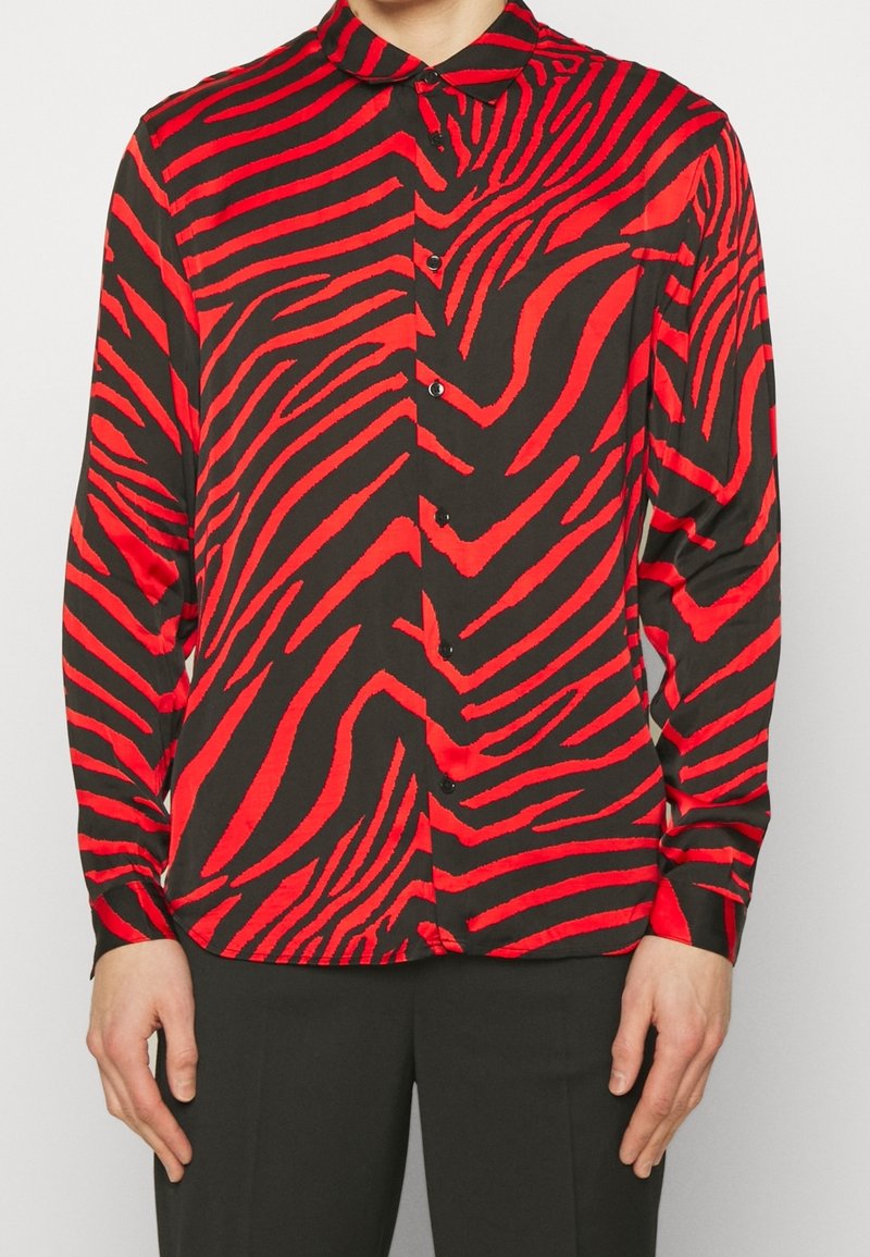 Camicetta a maniche lunghe rossa e nera con motivo a strisce zebrate, colletto e davanti con bottoni. Tessuto liscio con finitura lucida.