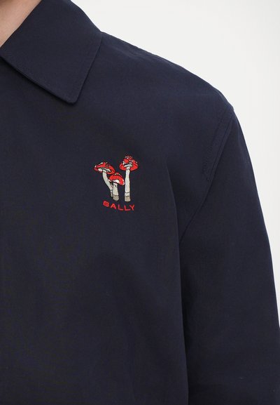 Camicia blu navy con colletto a punta e un evidente motivo ricamato di tre funghi rossi con steli grigi e la scritta "BALLY" in rosso.