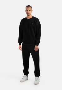 Felpa nera con scollatura a girocollo, tessuto morbido, polsini a costine e pantaloni jogger neri coordinati. Sneakers bianche completano l'outfit.