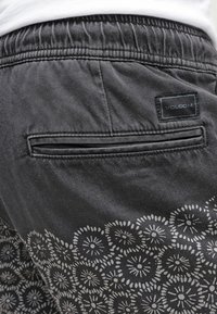 Black shorts with elastic waistband, featuring a back pocket and a white floral pattern along the bottom. Volcom label on the pocket.