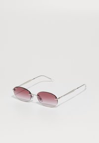 Lunettes de soleil avec un cadre en argent, des verres rectangulaires dégradés roses et des plaquettes de nez transparentes, reposant sur une surface blanche.