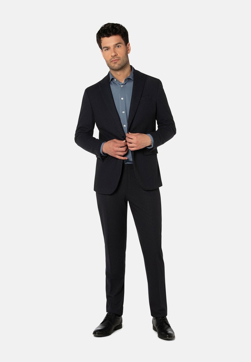Dunkelblauer Anzug mit einem taillierten Blazer und passenden Hosen, kombiniert mit einem hellblauen Button-Up-Hemd. Sanfte Textur und elegantes Design.