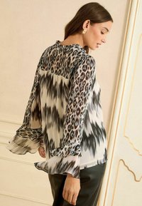 Könnyű, mintás blúz fekete és barna leopárdmintával, fodros mandzsettákkal és laza szabással. Átlátszó anyagú, áramló kialakítású.