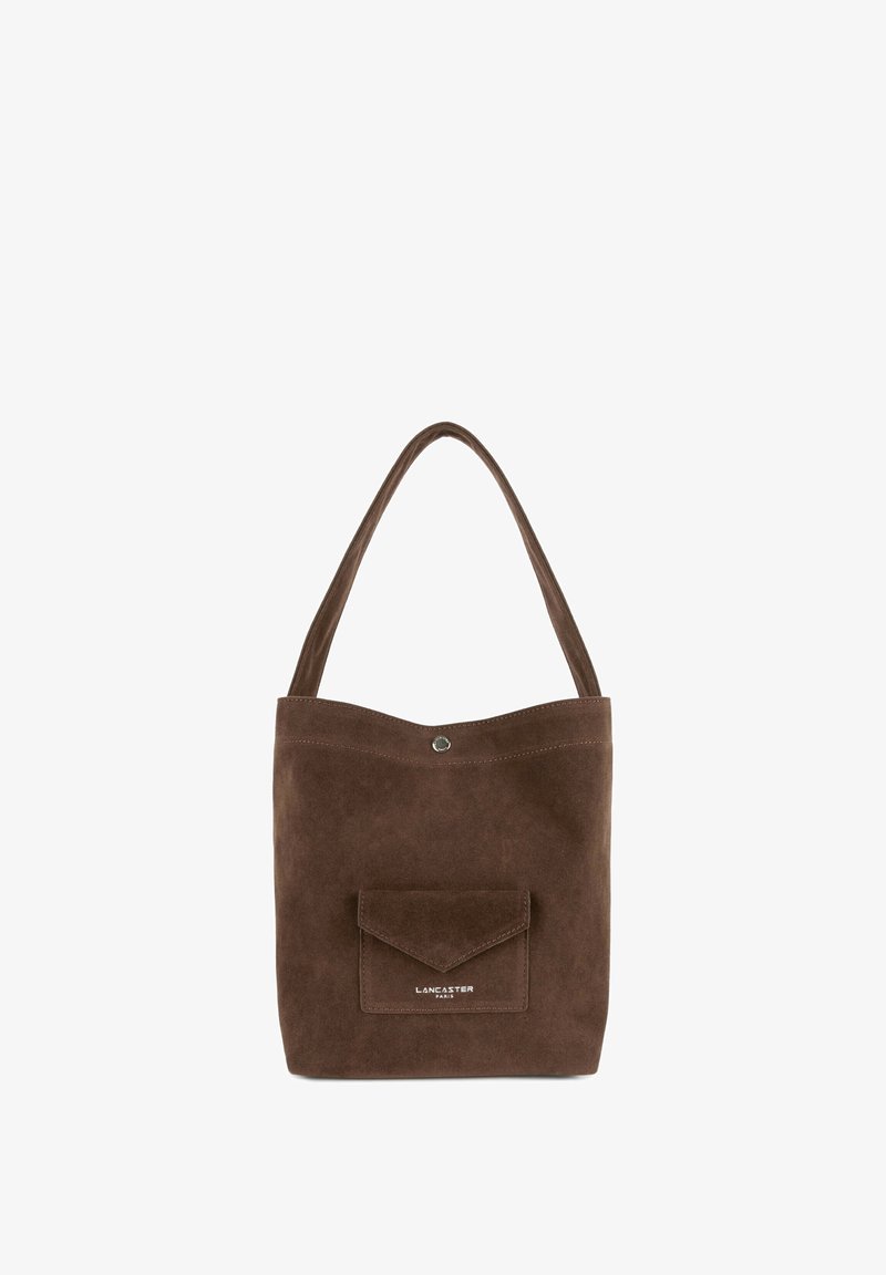 Sac fourre-tout en daim marron à texture lisse, avec un dessus incurvé et une poche frontale à rabat. Présente des ferrures argentées et un détail de logo.