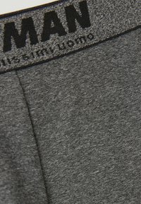 Cinturilla de mezcla de algodón gris con texto negro, que presenta una textura suave y un cuerpo gris sólido, diseñado para la comodidad y la flexibilidad.
