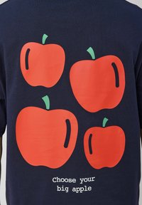 T-shirt bleu marine avec quatre grands motifs de pommes rouges avec des tiges vertes et un slogan en texte blanc, "Choisissez votre grosse pomme" en dessous.