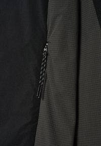 Nahaufnahme eines Reißverschlusses an einer schwarz-grauen Jacke mit doppelt ausgeführten Zuglaschen und strukturiertem Stoff auf der grauen Seite.