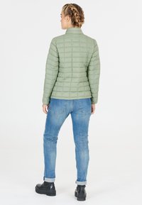 Ljusgrön quiltad jacka med ståkrage, i kombination med blå jeans och svarta klumpiga stövlar. Designen har horisontell sömnad.