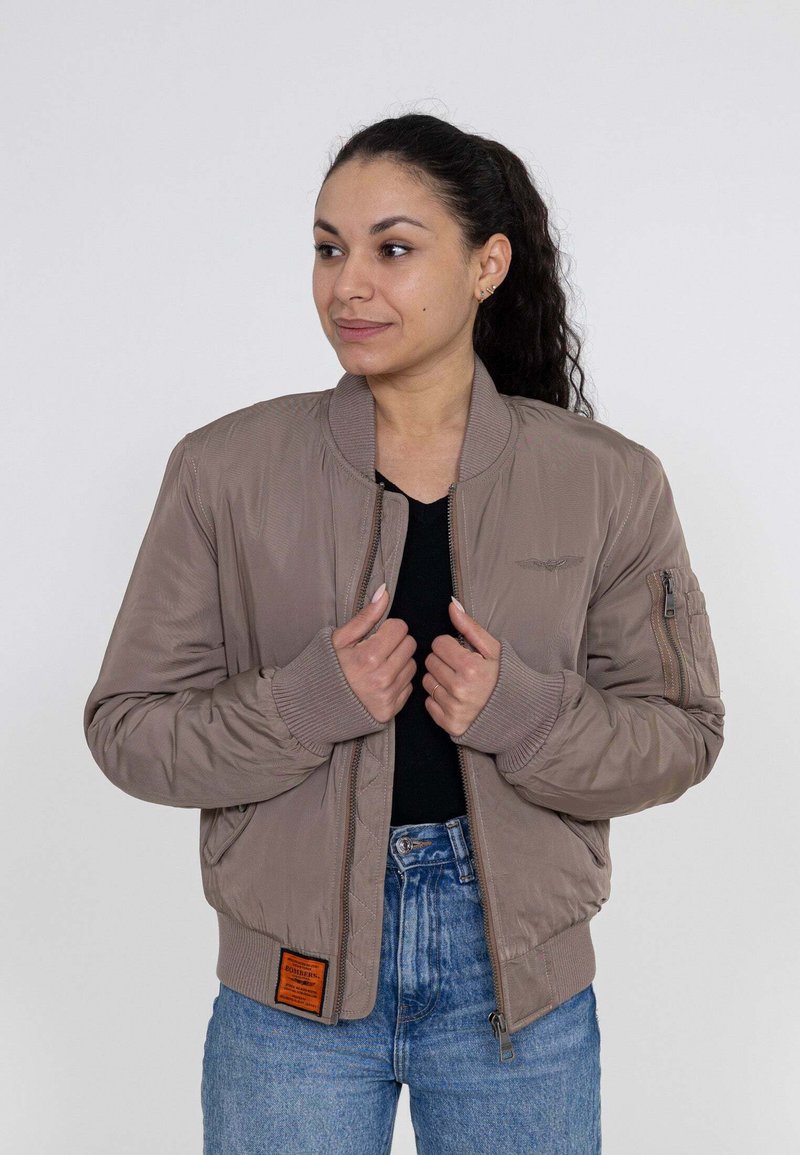 Giacca bomber marrone chiaro con polsini a coste, tasche con zip e texture trapuntata. Presenta un'etichetta del marchio arancione sull'orlo.