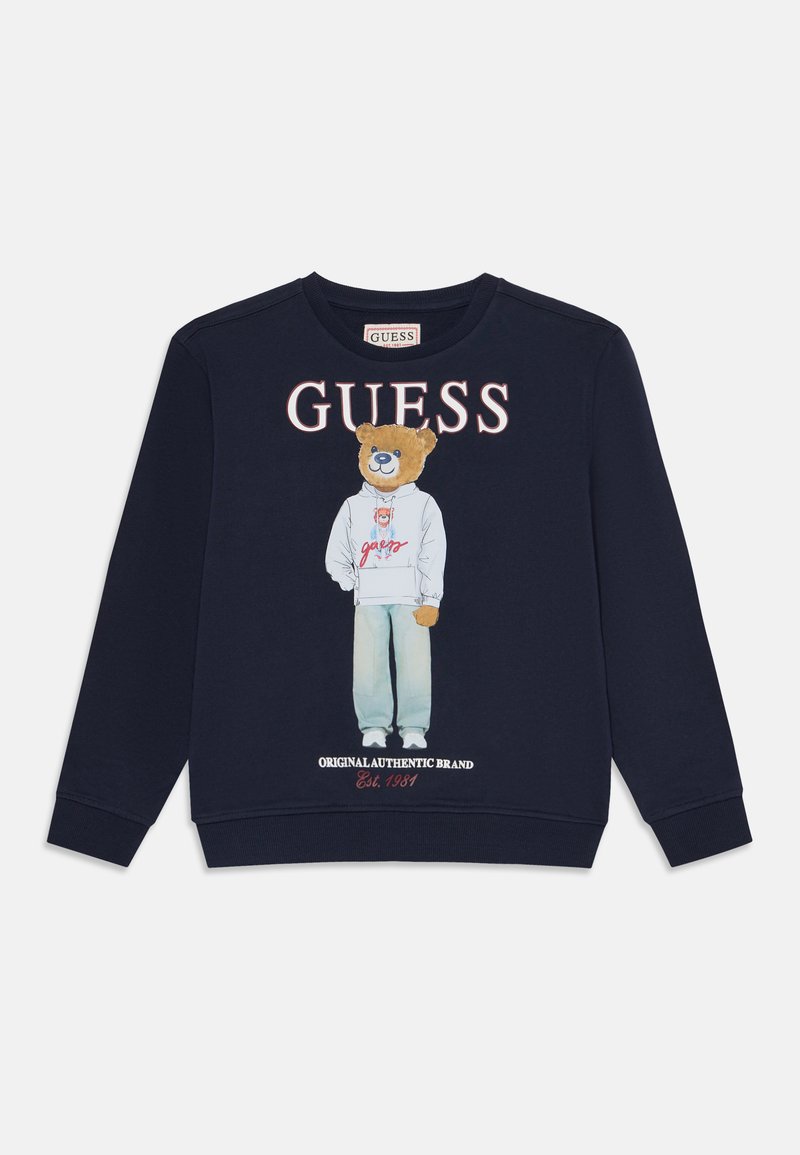 Sweat-shirt bleu marine avec un ours en peluche portant un sweat à capuche et un jean imprimé sous le grand texte "GUESS" et le texte plus petit "Original Authentic Brand Est. 1981".