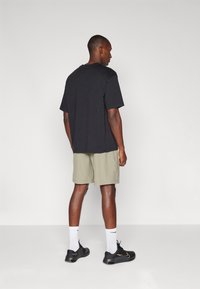 Zwarte T-shirt met korte mouwen, losse pasvorm, gecombineerd met lichtgrijze shorts. Zwarte sportschoenen en witte sokken met een zwart logo worden gedragen.