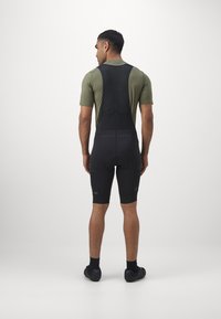 Zwarte fiets-bibshorts met een slimfit ontwerp, mouwloze top en gestructureerde bandjes. Bevat een gevoerd zitvlak en contrasterende logo-details.