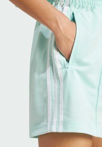 Pantalones cortos deportivos verde menta con franjas blancas a los lados, que incluyen un bolsillo lateral y una cinturilla elástica, fabricados con una tela suave y ligera.