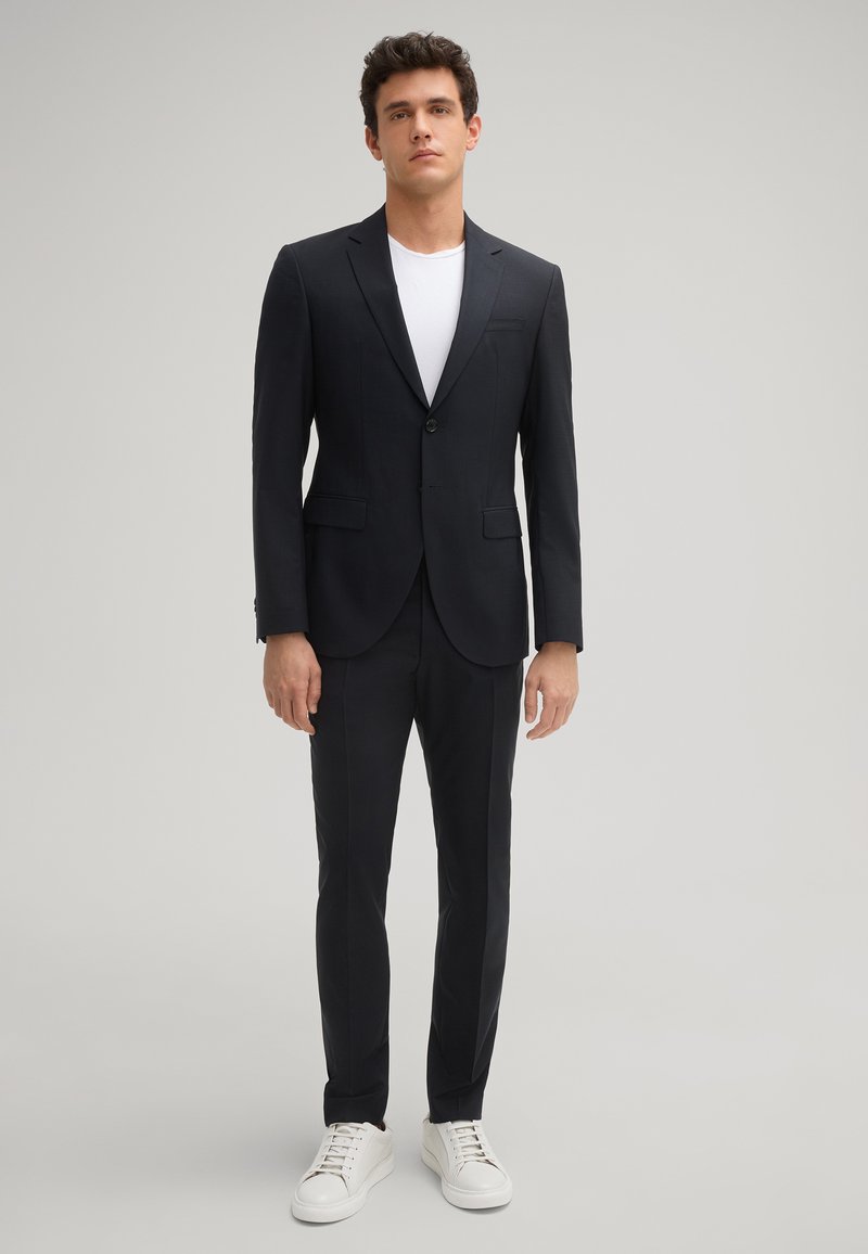 Marineblauwe blazer met notch-lapels en één knoop, gecombineerd met bijpassende broeken en witte sneakers. Glad materiaal met een gesneden pasvorm.