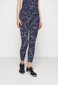 Collants azuis-marinho com padrões de linhas abstractas em rosa claro, material elástico, design justo e cintura alta, combinados com ténis pretos de desporto.