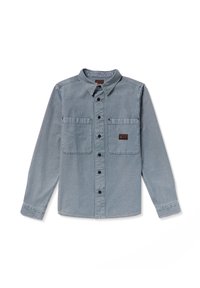 Camisa de manga larga y botón en denim azul claro. Presenta dos bolsillos en el pecho, botones negros y una etiqueta en el bolsillo derecho.