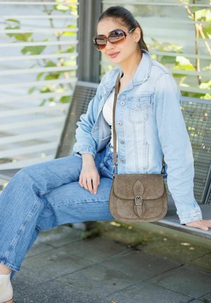 Braune Wildleder-Umhängetasche mit Klappe und Schnallenverschluss. Sie zeichnet sich durch eine glatte Textur und ein geschwungenes Design aus, das lässige Denim-Outfits ergänzt.