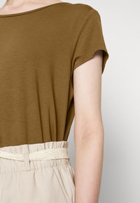 Olivově zelený krátký rukáv top s volným střihem, v kombinaci s béžovými kalhotami s elastickým pasem a tkaným opaskem. Hladká textura po celé ploše.
