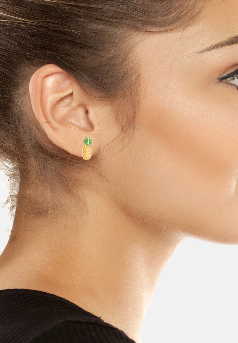 Gold-tone pineapple stud earrings with green leaf accents. Small, detailed design, set against a neutral skin tone and black top.