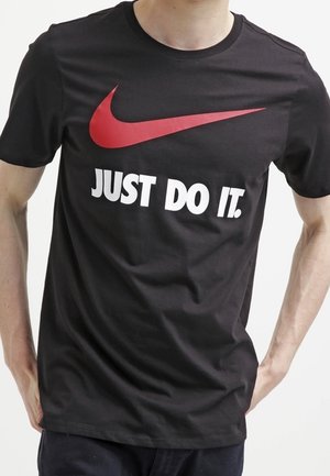 Personne portant un t-shirt noir avec un grand logo Nike swoosh rouge et un texte blanc disant "JUST DO IT."