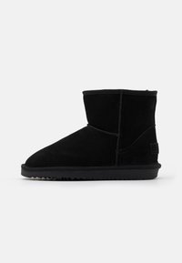 Stivale alla caviglia nero in morbida suede, con punta arrotondata, design cucito e suola in gomma testurizzata con un motivo a zigzag.