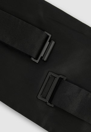 Sac en tissu noir avec deux sangles ajustables et quincaillerie métal noir. Présente une surface texturée et une forme plate et rectangulaire.