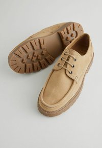 Zapatos de ante marrón con diseño de cordones, punta redonda y suela de goma con profundos relieves para un mejor agarre. Sencillos detalles de costura alrededor de los bordes.