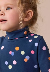 Mørkeblå højt halsen top med forskellige pastelfarvede polkaprikker i pink, orange og blå, lavet af blødt, strækbart bomuldsstof.