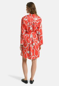 Abito in satin rosso con maniche lunghe, caratterizzato da un motivo marinaro di corde, conchiglie e ancore. Include una cintura in vita per definire la silhouette.