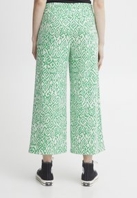 Gröna och vita mönstrade byxor med vida ben och elastisk midja; har geometriska mönster och sidofickor, samt svarta skor.