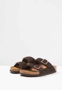 Sandali in suede marrone con due cinturini regolabili, soletta in sughero e suola in gomma testurizzata. Presenta dettagli metallici sugli cinturini.