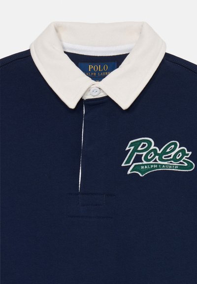 Polo shirt azul marino con cuello crema, que presenta un logo bordado en verde de "Polo" y una tapeta de dos botones, fabricado con suave tela de algodón.