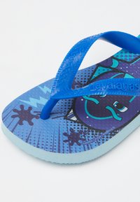 Modré žabky s texturovanou modrou podrážkou, které mají barevný grafický design a modré gumové popruhy. Světle modrá podrážka.